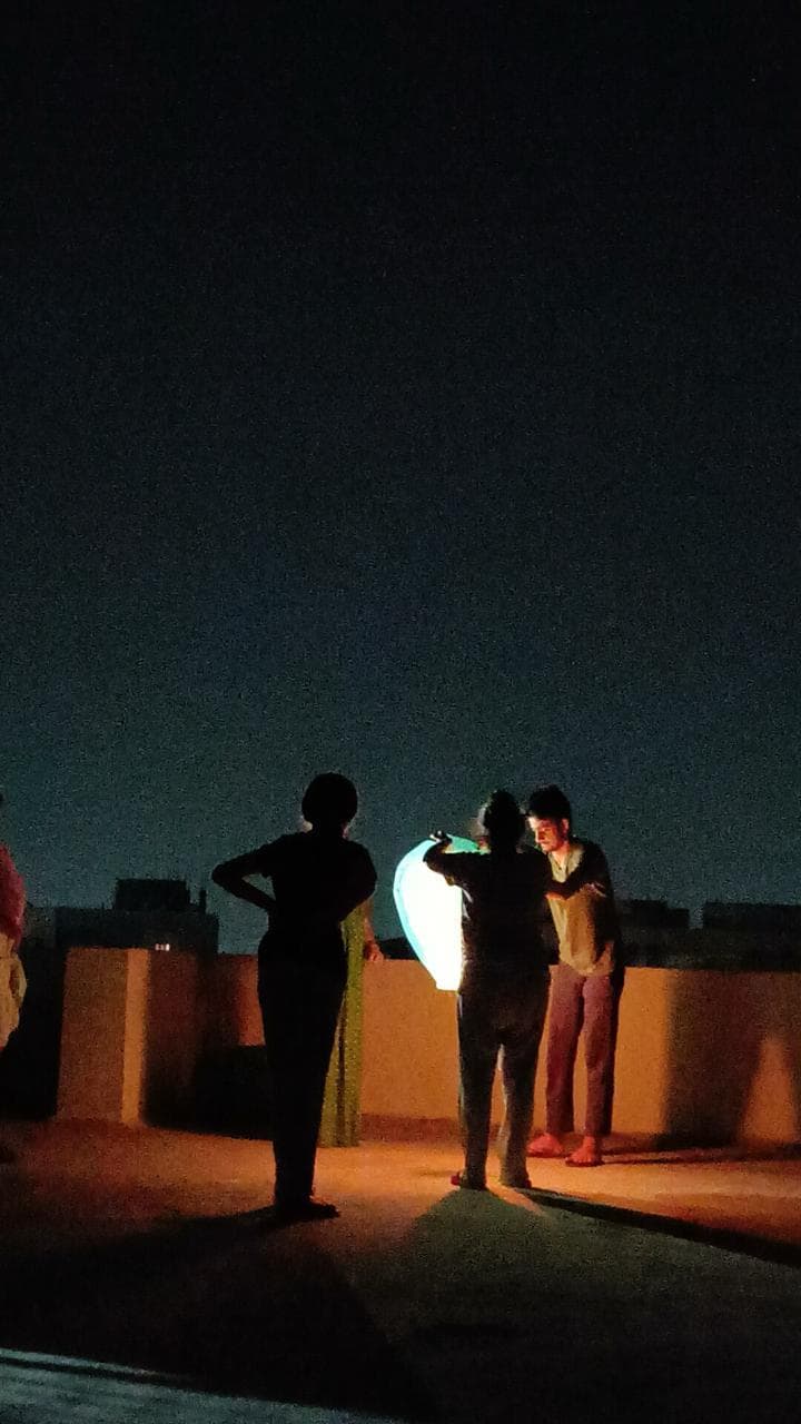 People on a rooftop at night, silhouetted around a glowing lantern.