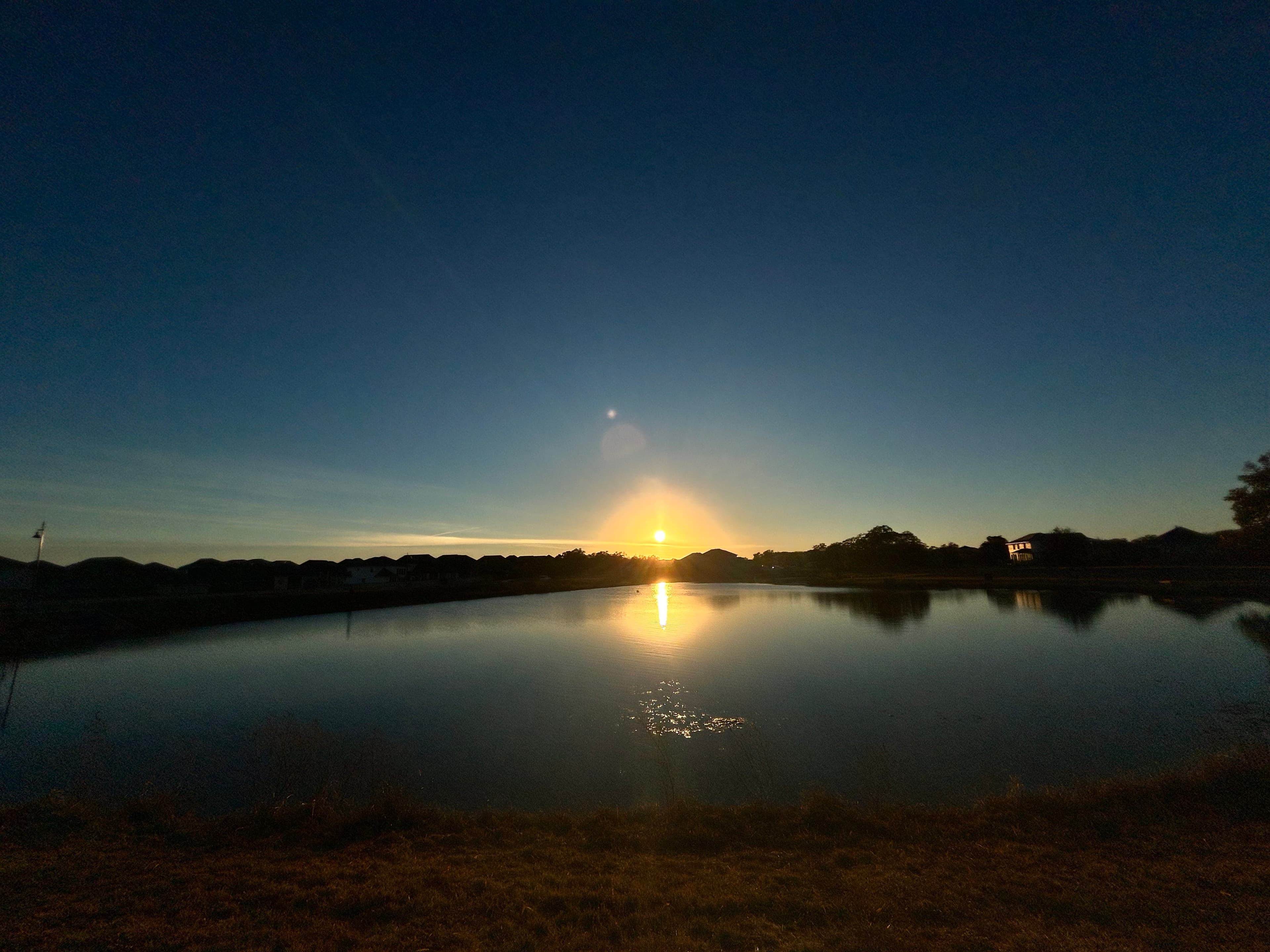A bright light in a deep blue sky reflected on a lake